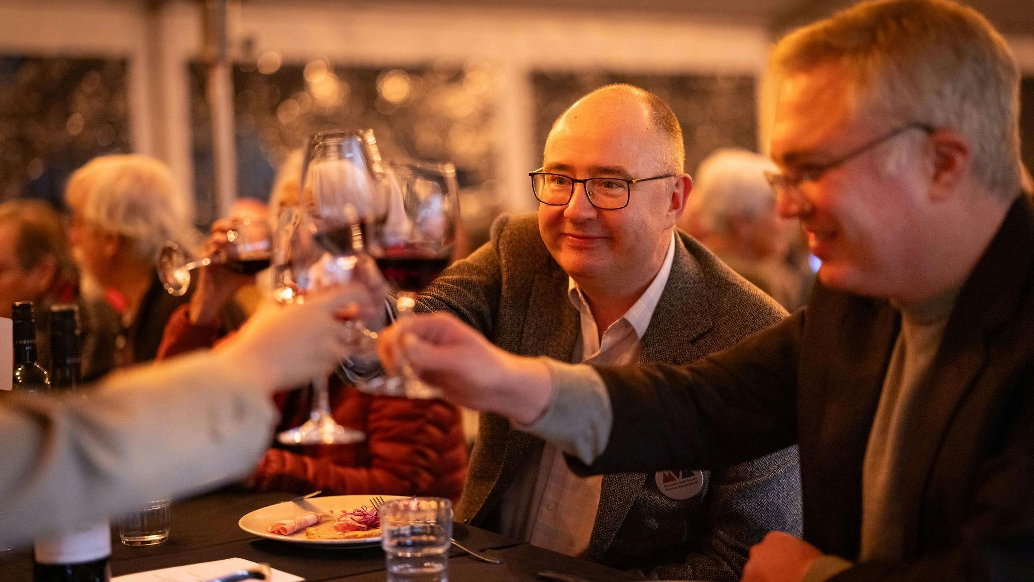 two men with glasses of wine toast the success of the music festival at the annual dinner