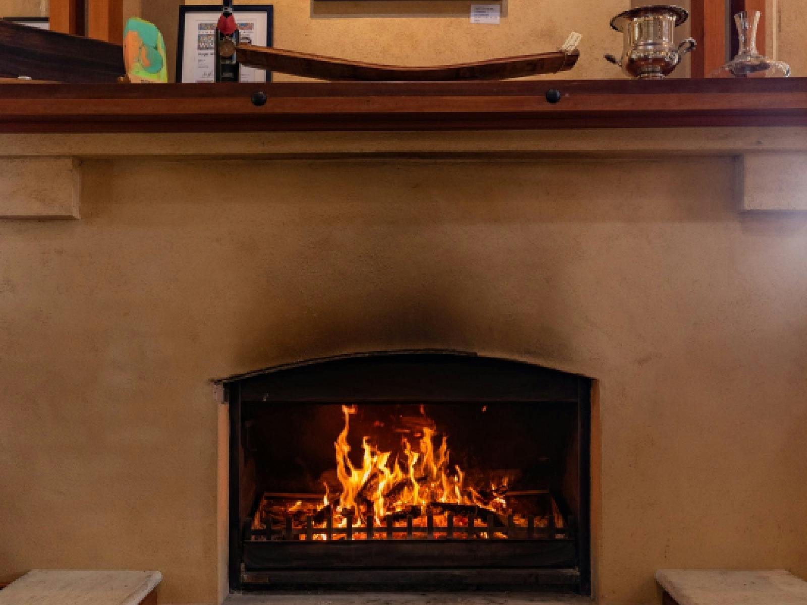 A roaring fire in a fireplace with a bottle of wine on the mantlepiece above