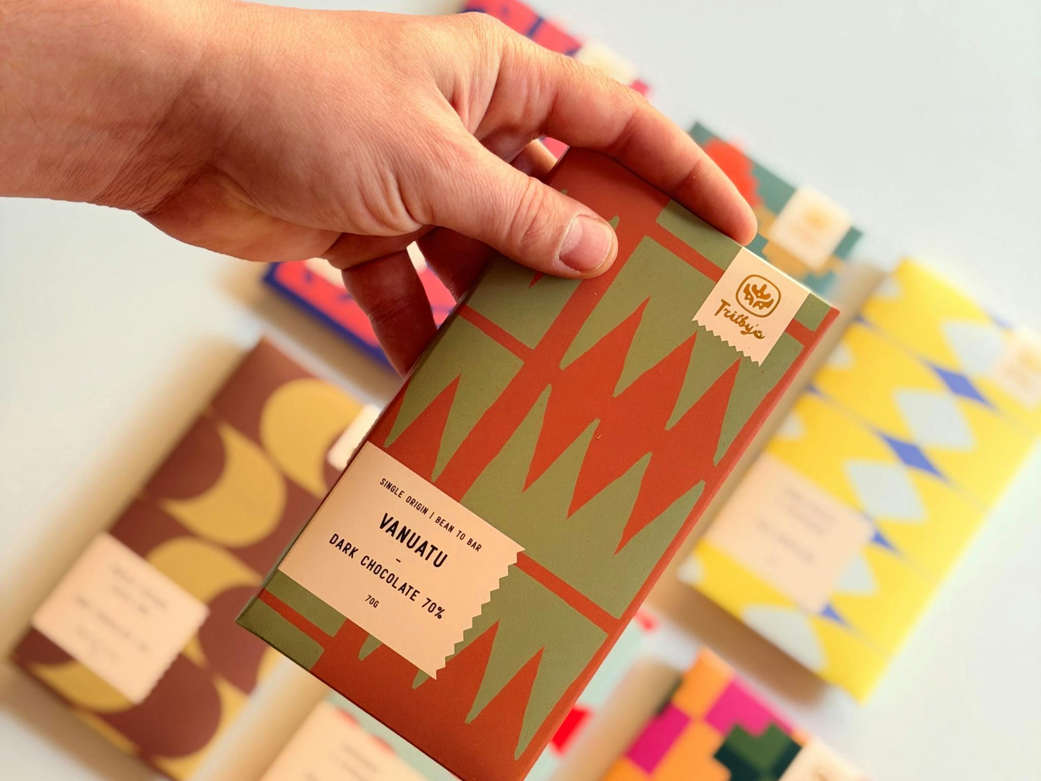 Hand holding a Vanuatu 70% Dark Trilby’s chocolate bar with others blurred behind.