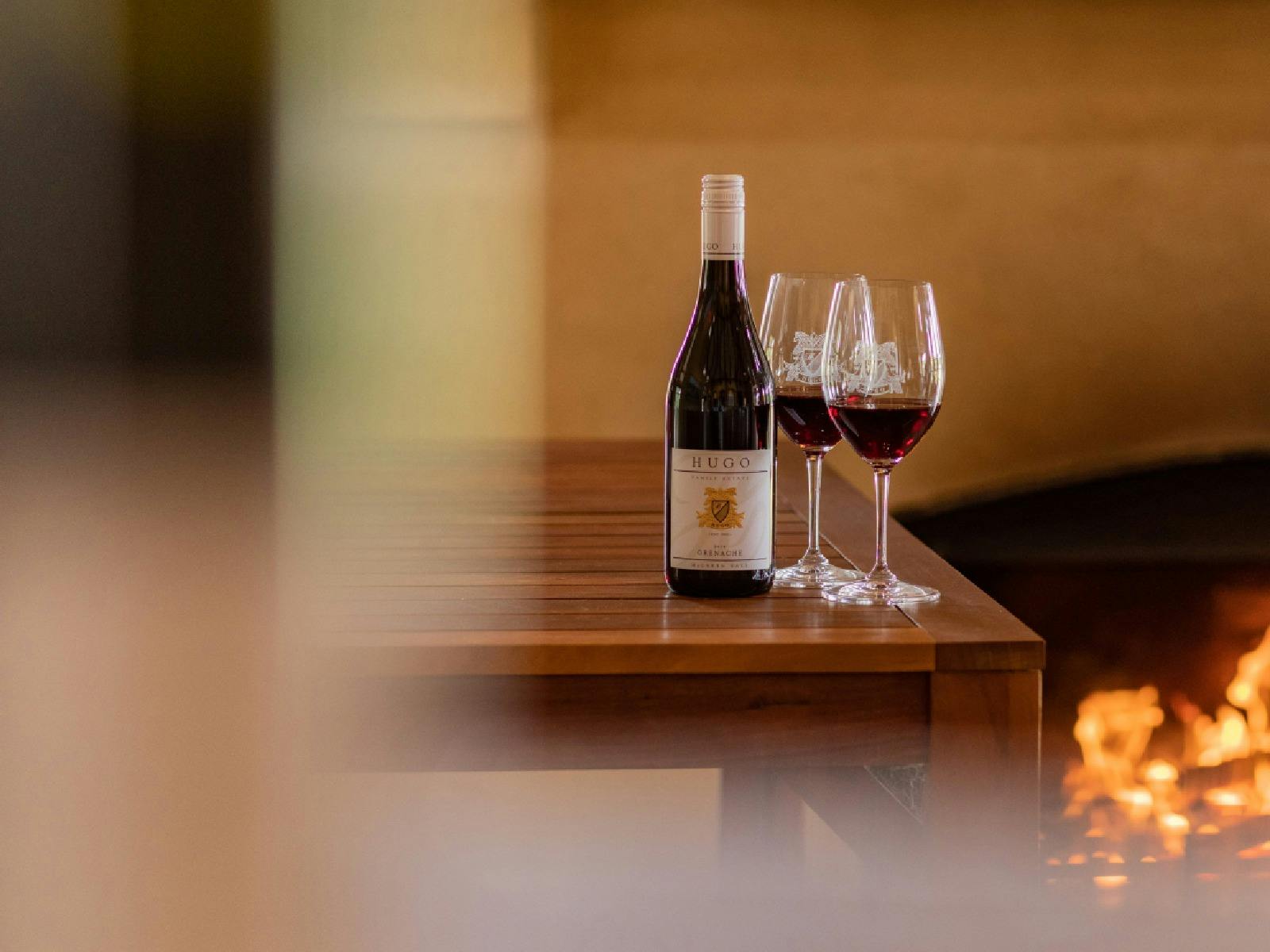 A bottle of red wine and 2 wine glasses with a fireplace in the background