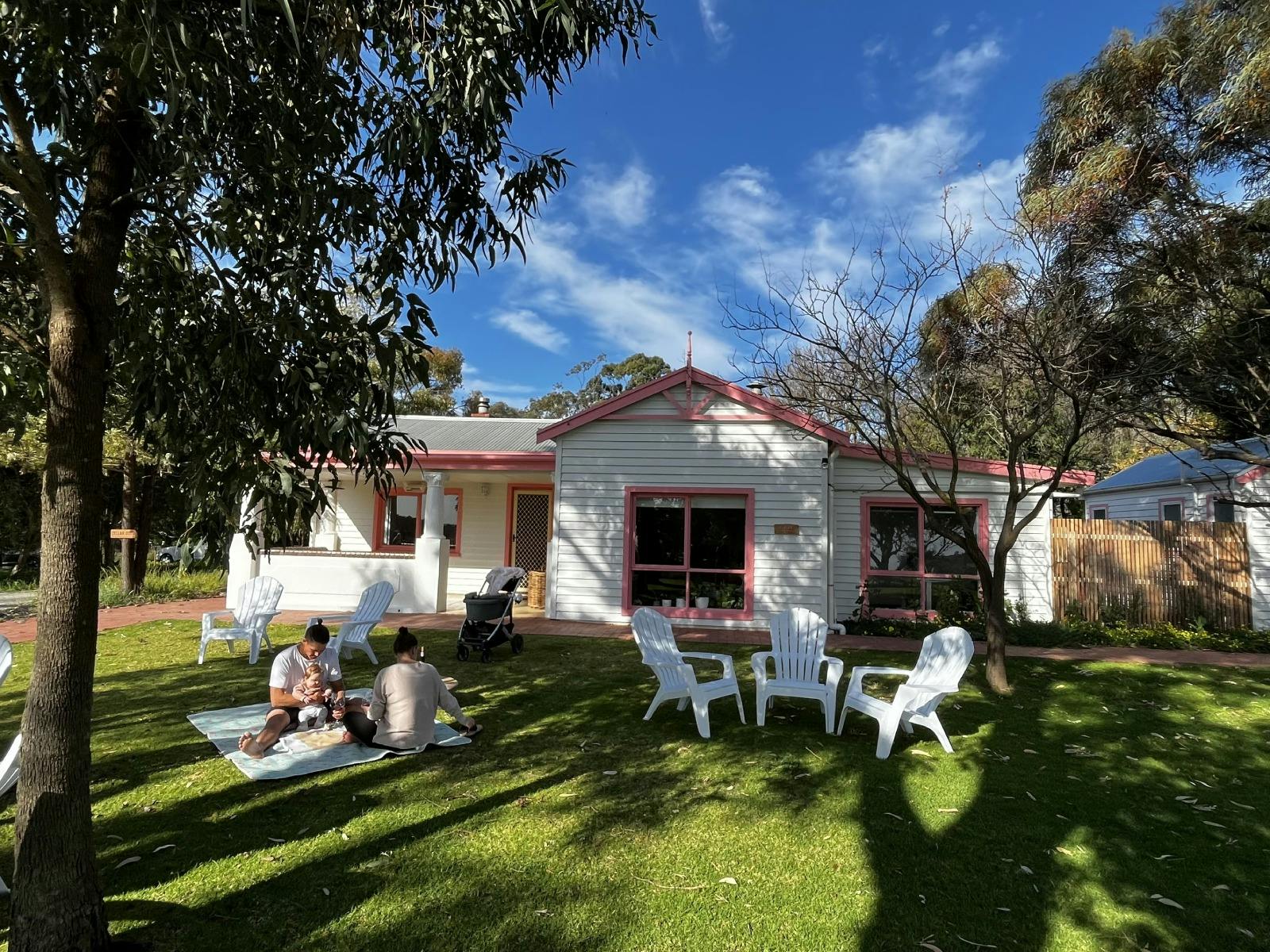 A couple seated on a picnic rug, with Somos Wine Cellar Door in the background