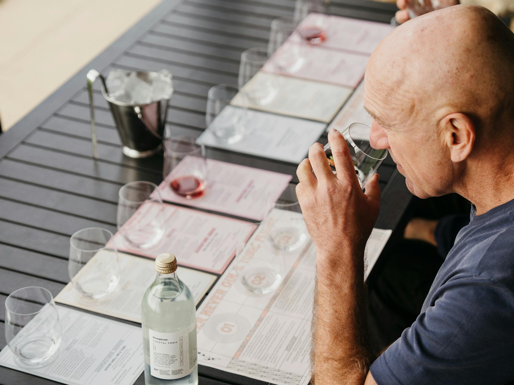 Man smelling a gin with a tasting panel in front of him on a black table.