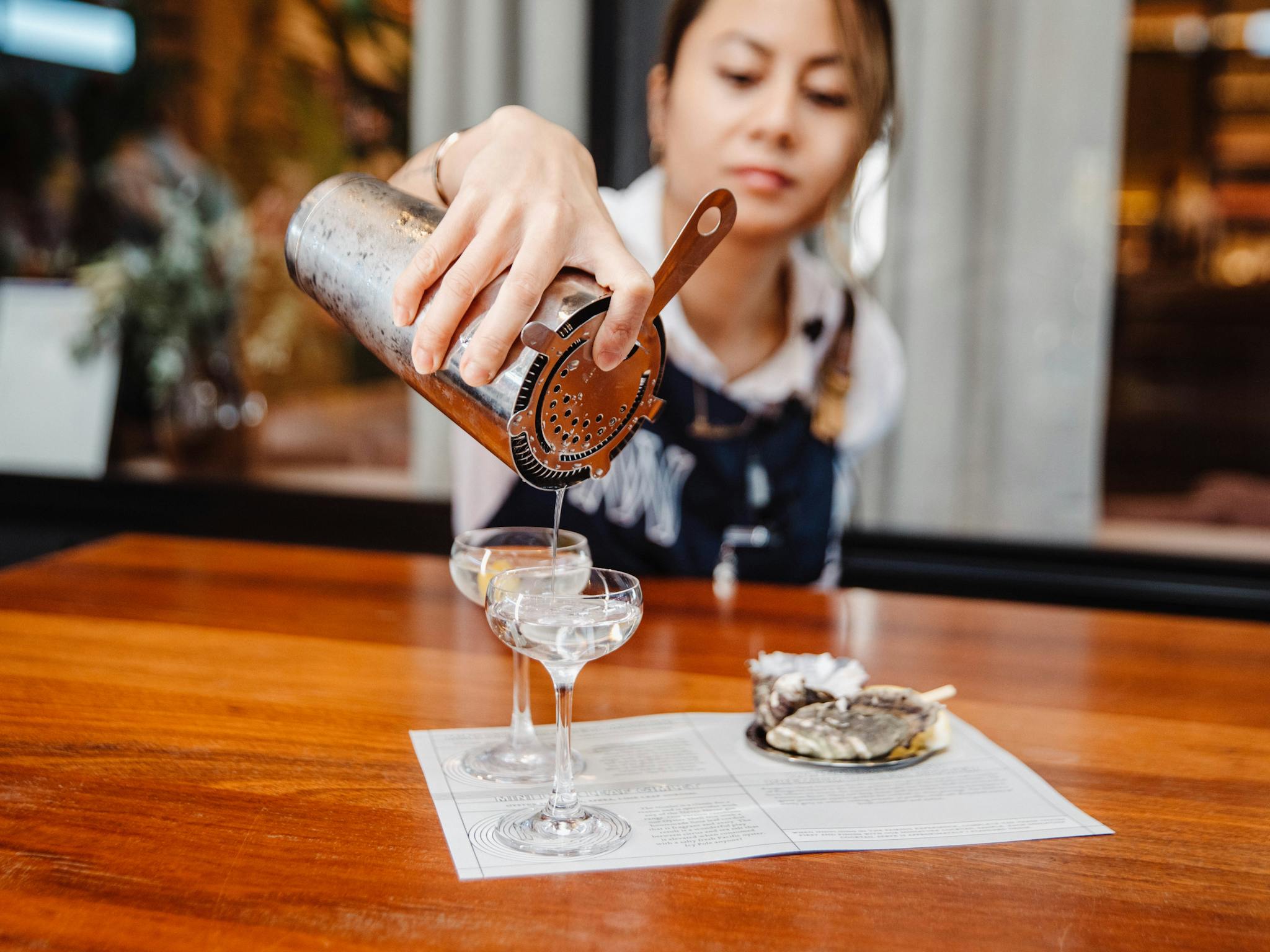 Bartender pours a cold martini into a mini glass next to an oyster