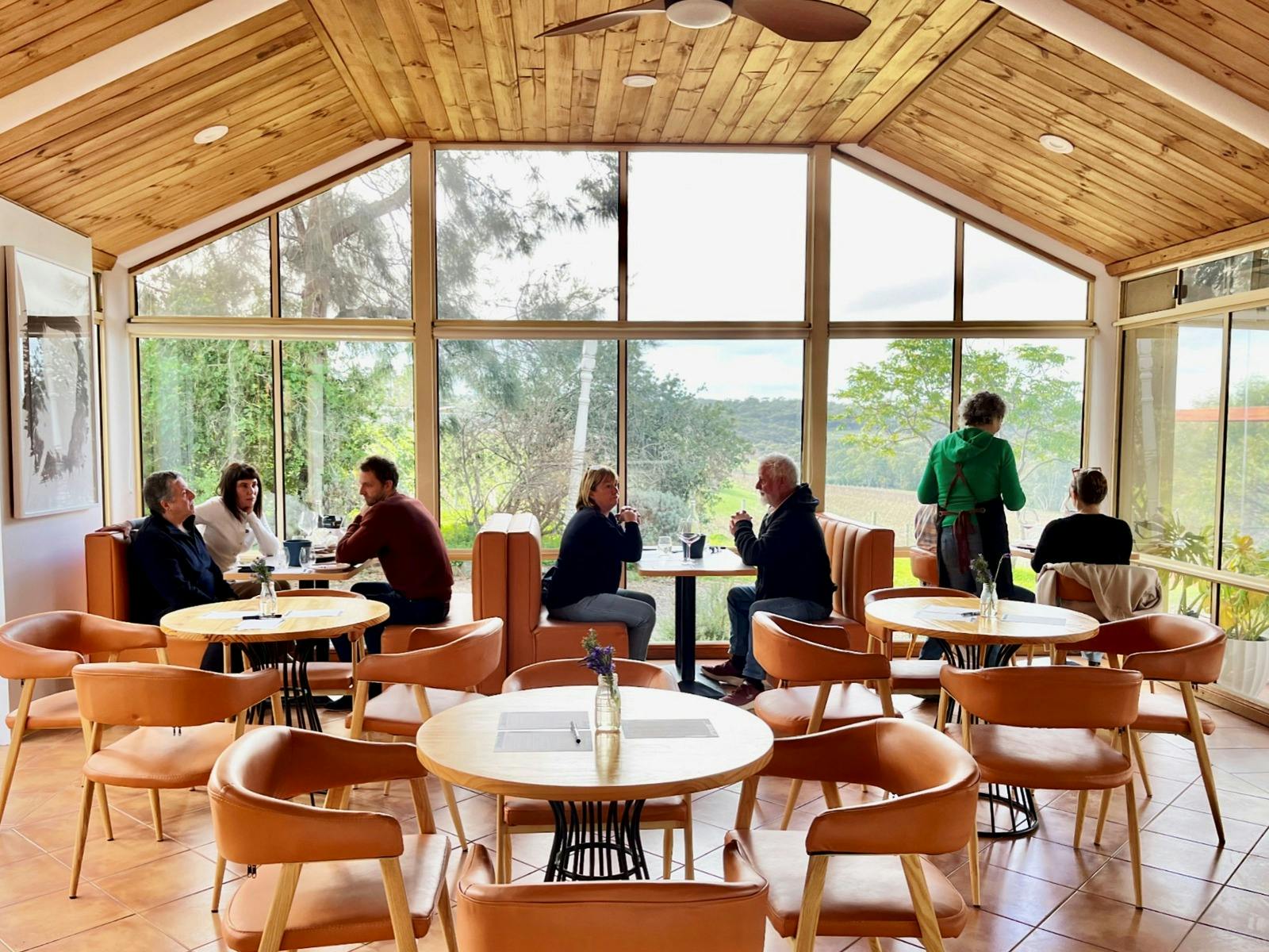 People sitting at tables sipping wine near a window overlooking vineyards