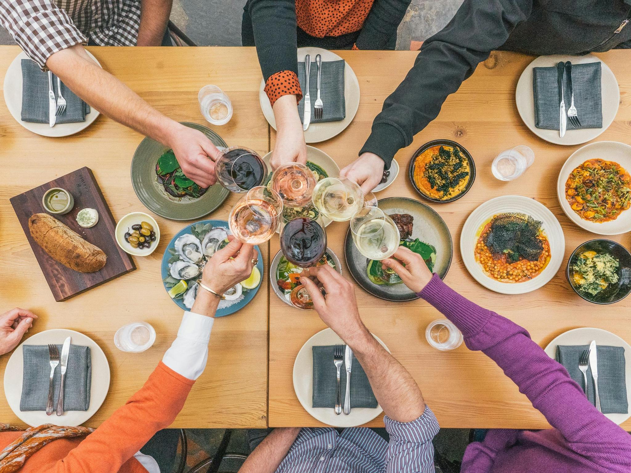 A table filled with food, wine glasses overhead cheers-ing.