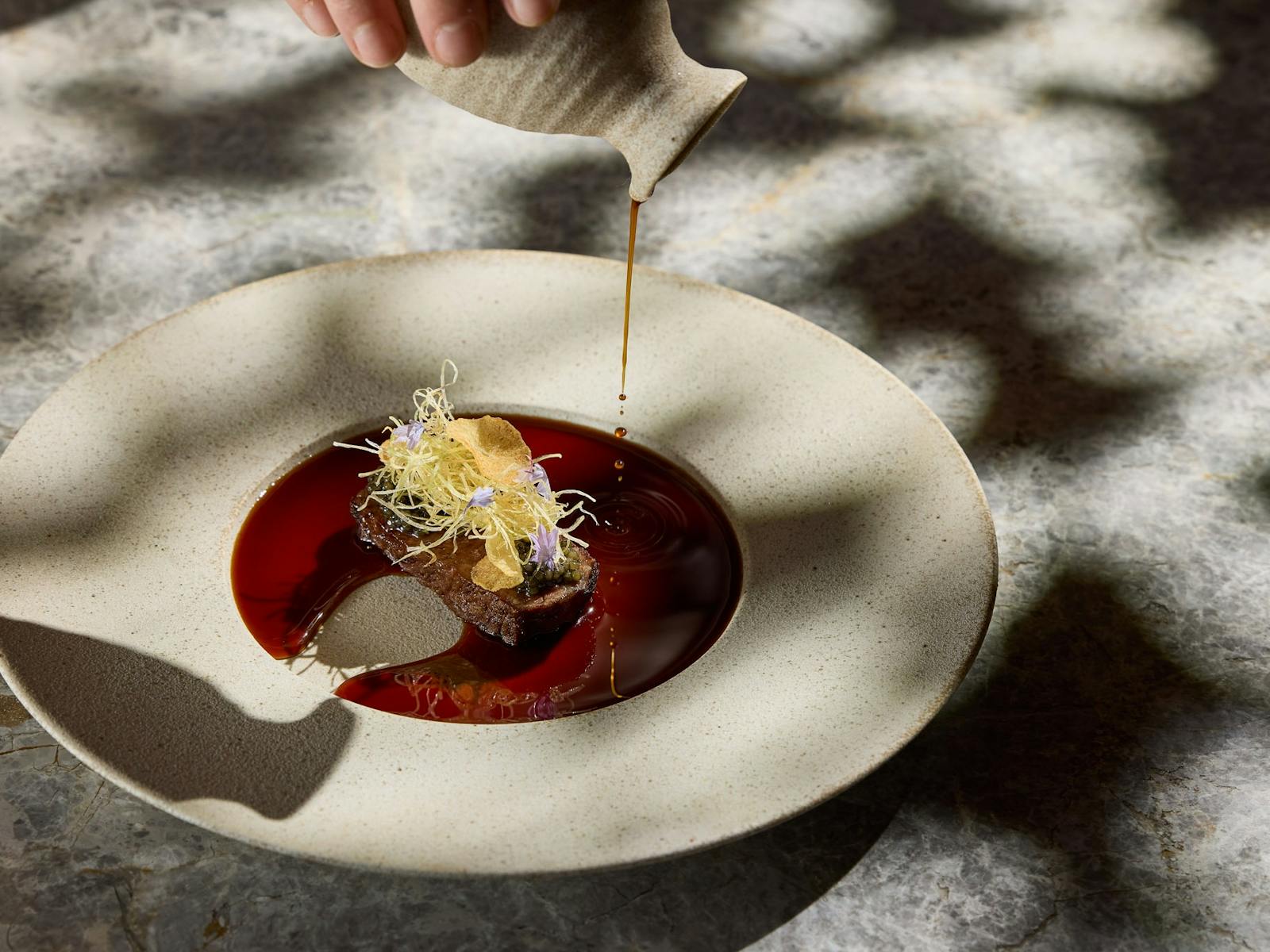 A piece of beef, garnished with fried leek and garlic chips, and surrounded by rich beef jus.