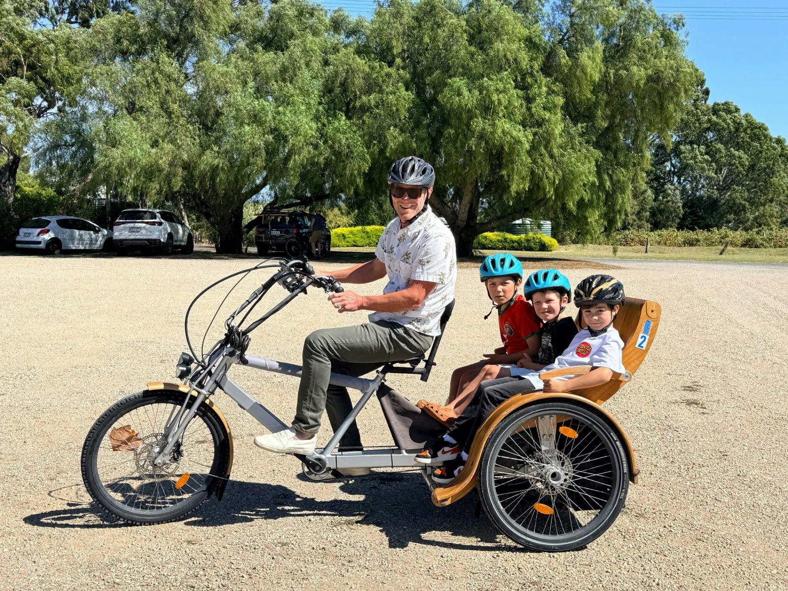 A man riding a TukTuk with 3 children in the seat behind at Hugo Wines