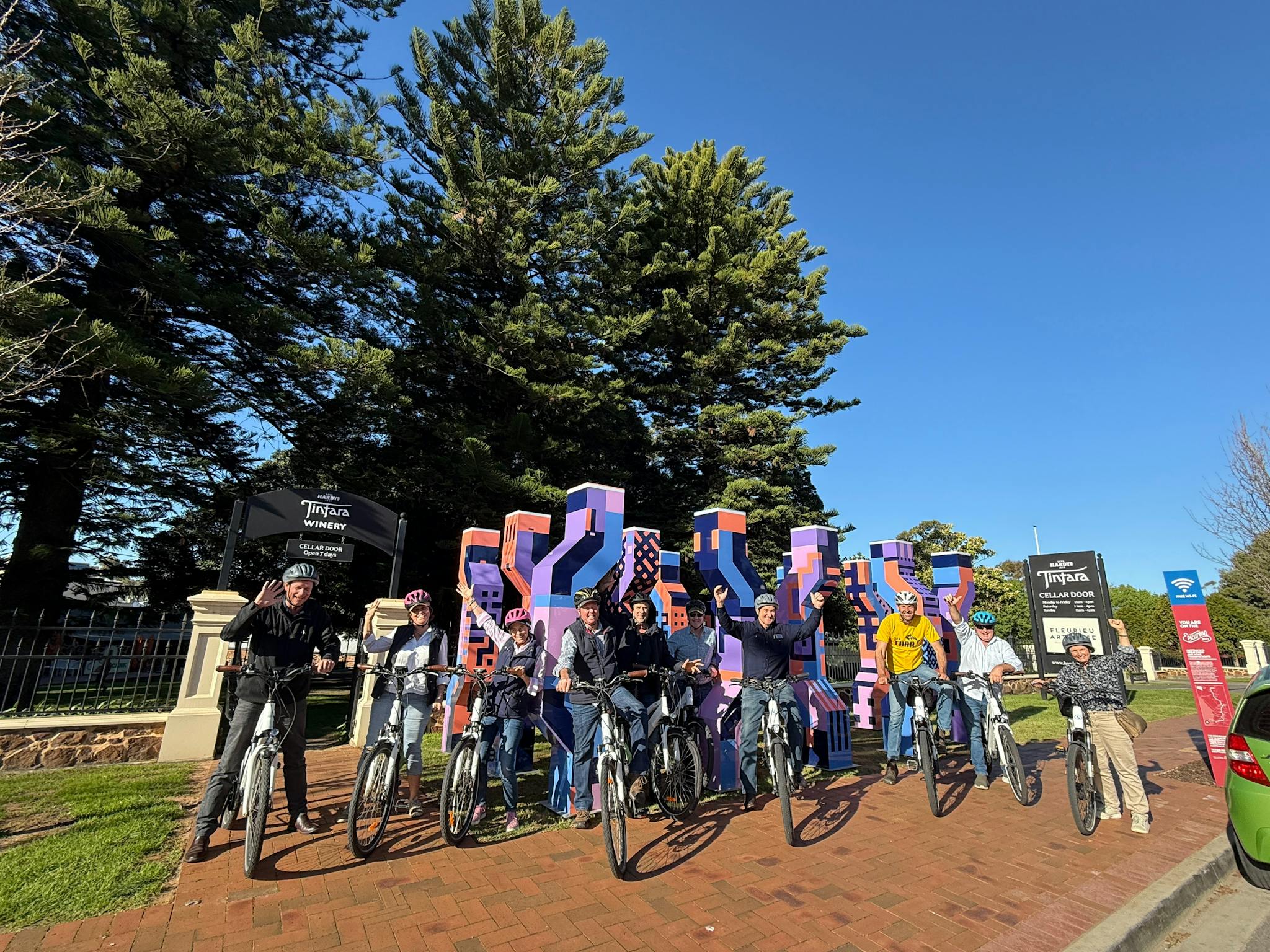 A group of eBike riders posing in front of the purple sculptures in Main St. McLaren Vale