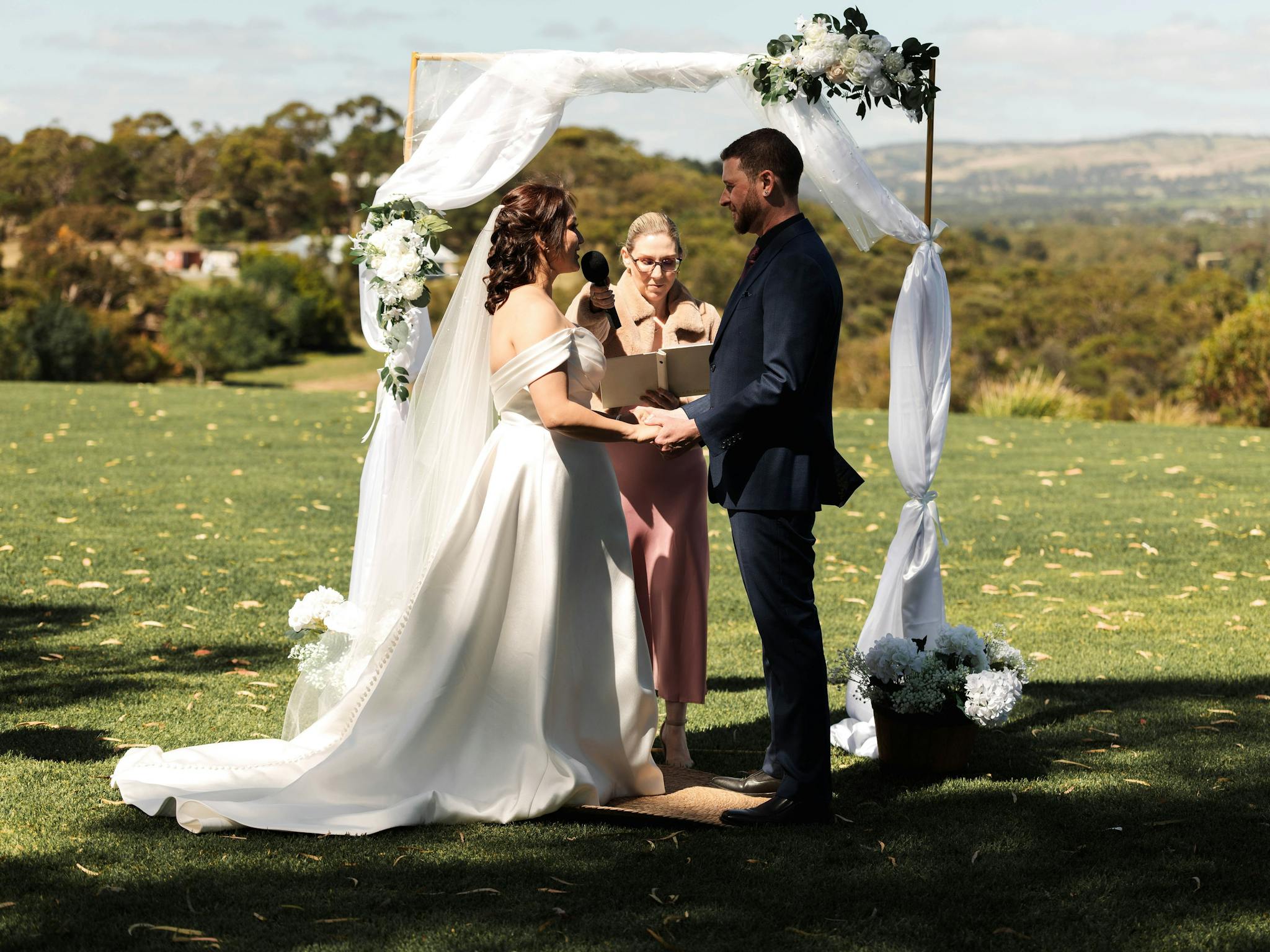 Couple being married in front of a gold arbour with hills in the background
