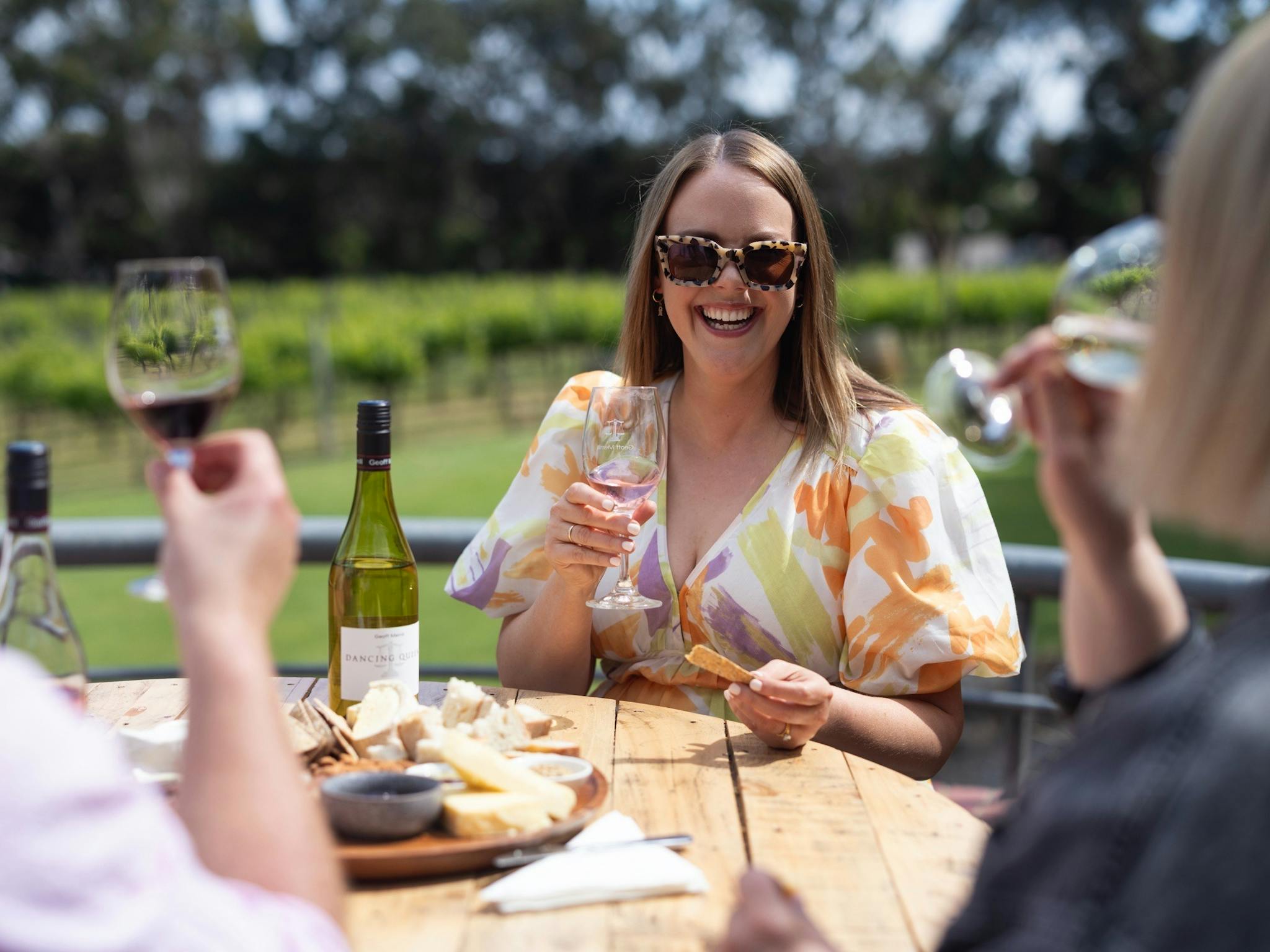 A woman with sunglasses holding a wine and smiling